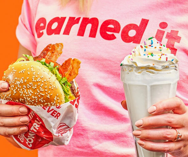 Person wearing &quot;earned it&quot; t-shirt holding a Bacon Cheeseburger and Chocolate Shake