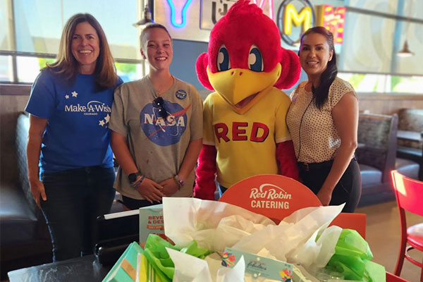 Young girl enjoying her wish reveal with Red Robin mascot and friends