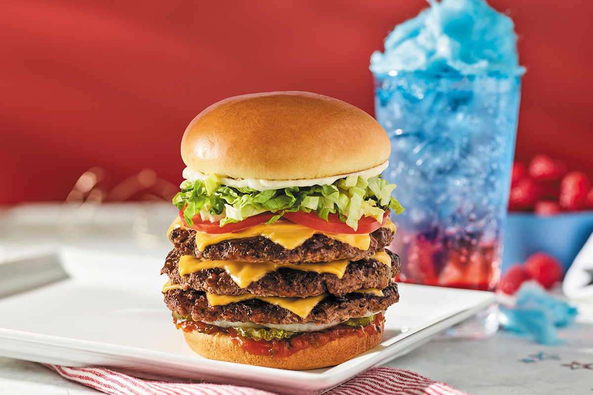 Burger with three patties and drink in the background