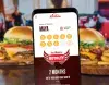 Red Robin mobile app displaying burger tracker on phone, in front of two plated burgers in restaurant