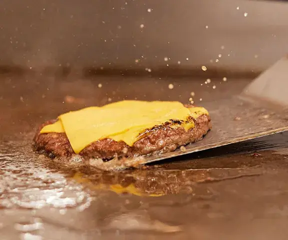 Beef patty with cheese on flat top grill