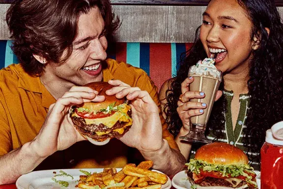 Man eating a burger and woman eating a shake