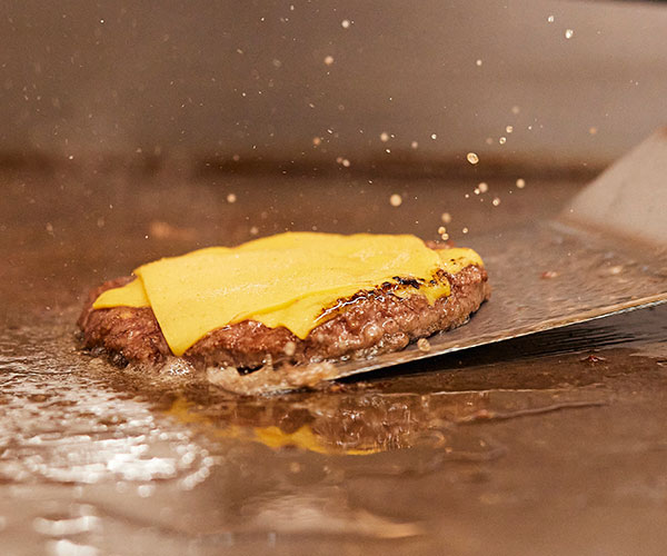 Beef patty with cheese on flat top grill